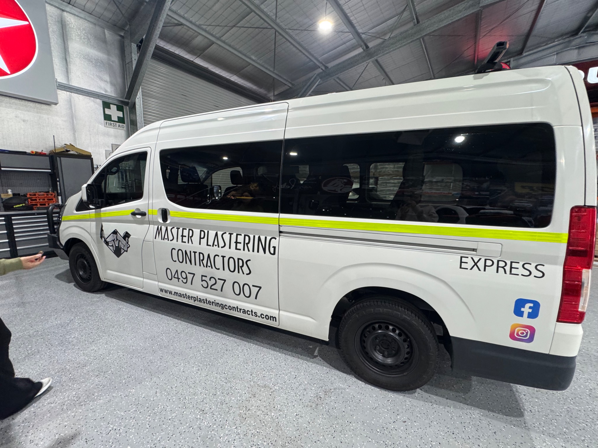 White Master Plastering Contractors crew minibus with a yellow stripe, parked in a workshop